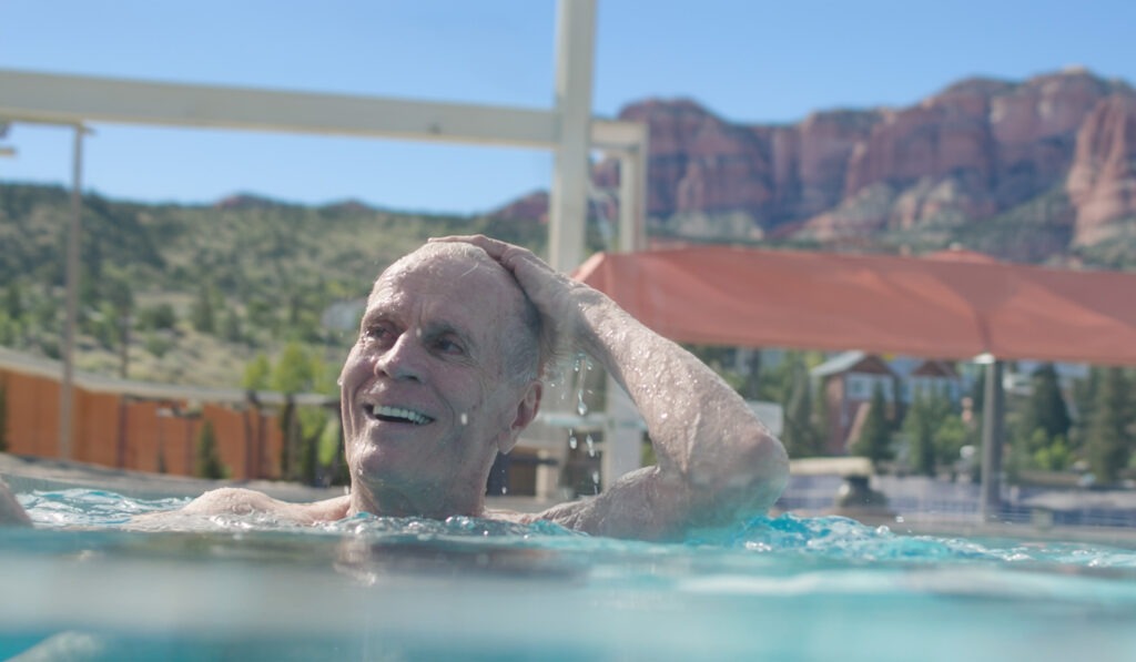 Goldstream_Swimming_Redrock-background - Snow Canyon Older man enjoying a swim with scenic red rock views at Snow Canyon Retirement Community, offering vibrant senior living near St. George, Utah.