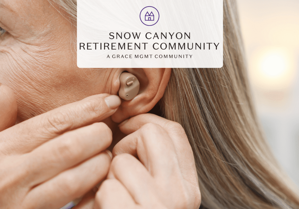 Close-up of an elderly person inserting a beige hearing aid into their ear with a caregiver's touch nearby.